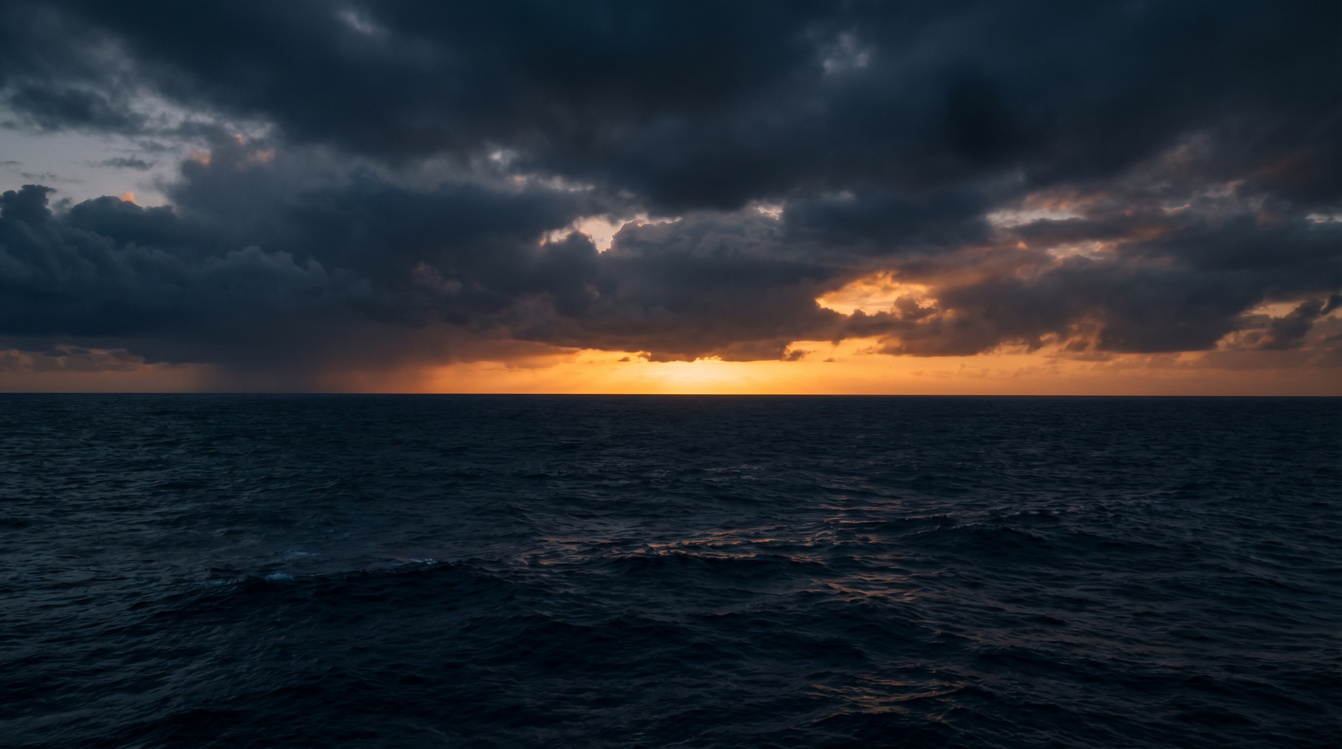 Open ocean at dusk — dark sea, dramatic amber horizon